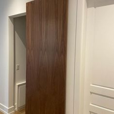 an empty room with white walls and wooden door in the center, along with hardwood flooring