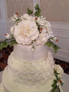 a three tiered wedding cake with white flowers on the top and green leaves around it