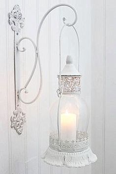 a candle is lit in a glass lantern hanging from a hook on a white wall