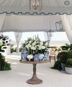 a table topped with vases filled with flowers under a white tent covered by curtains