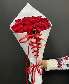 someone holding a bouquet of red roses on a black table with white wrapping around it