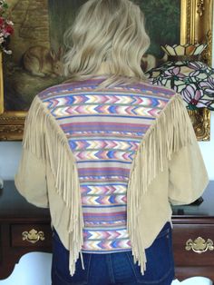 a woman standing in front of a painting wearing a jacket with fringes on it