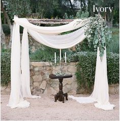 an outdoor ceremony with white draping and greenery on the altar, surrounded by stone walls