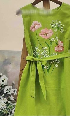 a green dress with pink and white flowers painted on the front, tied to a wooden hanger