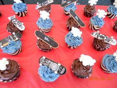 cupcakes with blue frosting and snowboards on them sitting on a red tablecloth