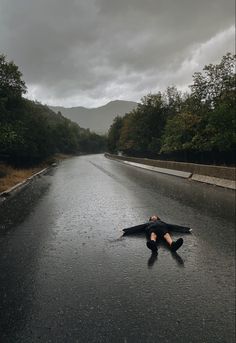 a man laying on the side of a wet road in the middle of the day