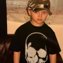 a young boy wearing a camo hat standing in front of a brown leather couch