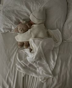 a teddy bear laying on top of a bed covered in white sheets and blanketes