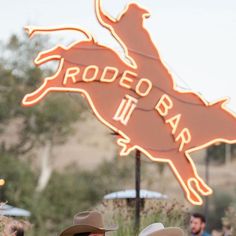 two men in cowboy hats standing next to a rodeo bar sign with horses on it