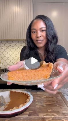 a woman holding up a pie in her hands while sitting at a kitchen table with an empty plate