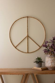 a peace sign hanging on the wall next to a potted plant and vase with purple flowers