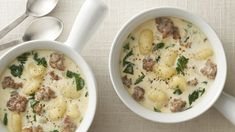 two white bowls filled with soup next to spoons