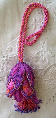 a pink and purple handbag with tassels on a white lace tablecloth