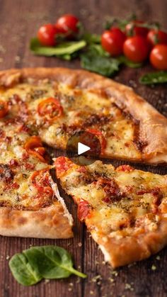 a pizza cut into four slices on top of a wooden table next to tomatoes and basil