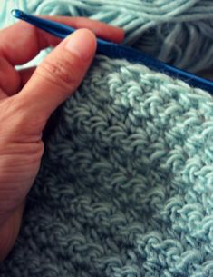 a person is crocheting the ends of a knitted blanket with a blue knitting needle