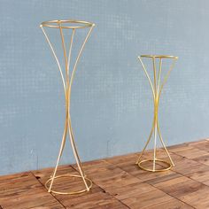 two gold metal vases sitting on top of a wooden floor