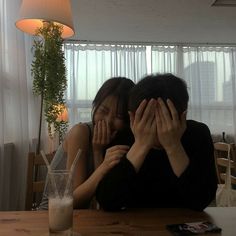 two people covering their faces while sitting at a table with drinks in front of them