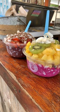 two plastic bowls filled with fruit and ice cream on top of a wooden countertop