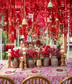 a table topped with lots of vases filled with red flowers and hanging bells above it