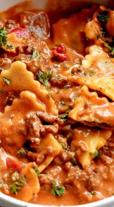 a white bowl filled with pasta and meat covered in sauce, garnished with parsley