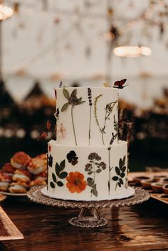 a wedding cake decorated with flowers and leaves on a table in front of other desserts