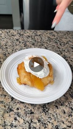 a white plate topped with a pastry on top of a counter next to a woman's hand