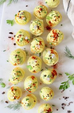 deviled eggs with sprinkles and herbs on a white surface next to spices