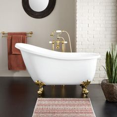 a white bath tub sitting on top of a hard wood floor next to a brick wall