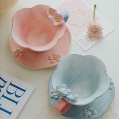 two pink and blue dishes sitting on top of a table next to a magazine with flowers