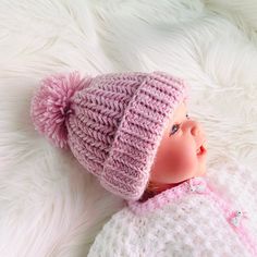 a baby doll wearing a pink knitted hat laying on top of a white blanket