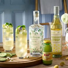 several different types of alcohol on a table with cucumbers and flowers in the background