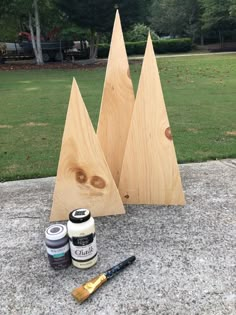 two wooden trees are sitting on the ground next to some paint and brush, along with other woodworking supplies