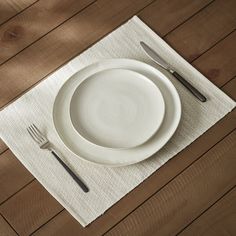 a white plate and silverware on a placemat with a wooden table in the background