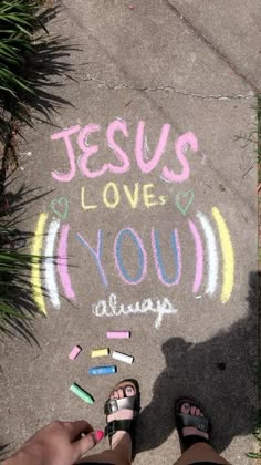 someone's feet with crayons in front of the chalk drawing jesus loves you always