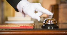 a hand in white gloves is on top of a desk with a book and a bell