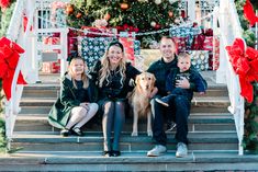 a family sitting on the steps with their dog in front of a christmas tree and presents