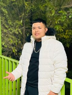 a man wearing a white jacket and black shirt standing in front of a green railing