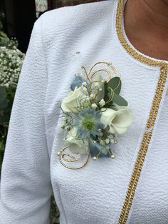 a woman wearing a white jacket and holding a flower brooch in her left hand