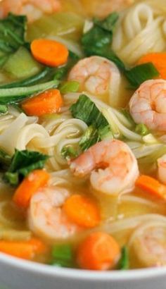 a white bowl filled with shrimp, noodles and veggies in broth next to carrots