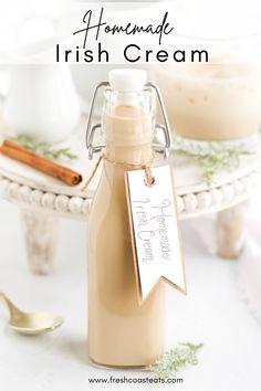 homemade irish cream in a glass bottle on a white table with cinnamon sticks and spoons