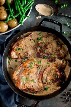 pork chops with gravy in a skillet next to green beans and potatoes