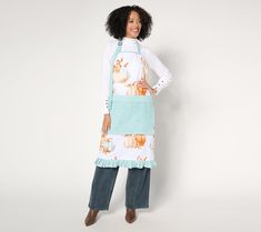 a woman standing in front of a white wall wearing an apron with pumpkins on it