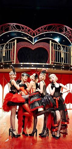 four women dressed in red and black are posing for a photo on stage with their legs crossed