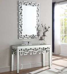 a white console table with a mirror and vase on it in front of a window