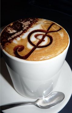 there is a cup of coffee with music on it and spoon next to the cappuccino