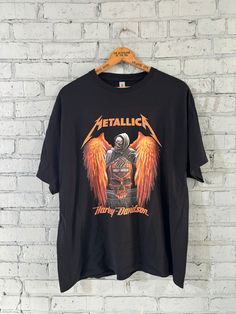 a black metallichead t - shirt hanging on a brick wall with an orange angel