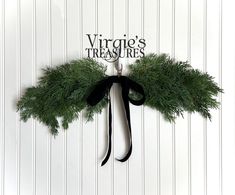 a green wreath hanging on the side of a white wall with black ribbon and words virginia's treasures