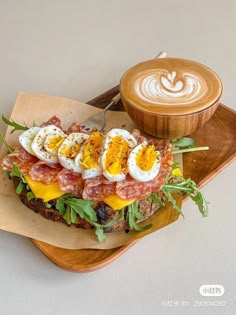 a sandwich with eggs, bacon and cheese on it next to a cup of cappuccino