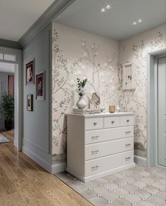 a white dresser sitting inside of a bedroom next to a wallpapered wall with flowers on it