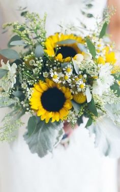 a bride holding a bouquet of sunflowers and greenery